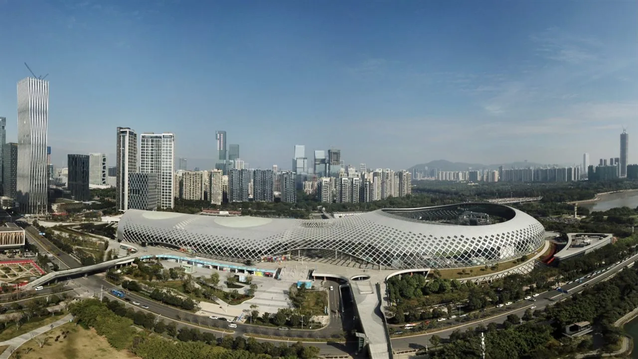 The Shenzhen Bay Sports Center, a low latticed dome nicknamed the Spring Cocoon, seen from the air with the Nanshan skyline behind