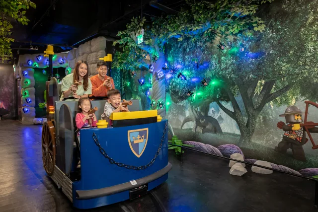 Una familia en un vehículo de Kingdom Quest junto a las dianas iluminadas de la atracción