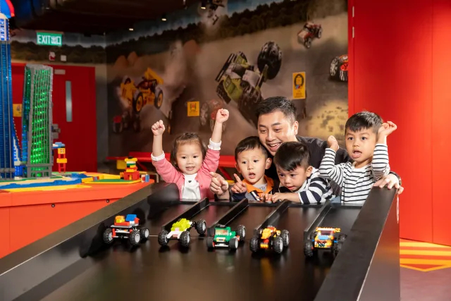 Varios niños y un adulto observando coches LEGO en una rampa de pruebas